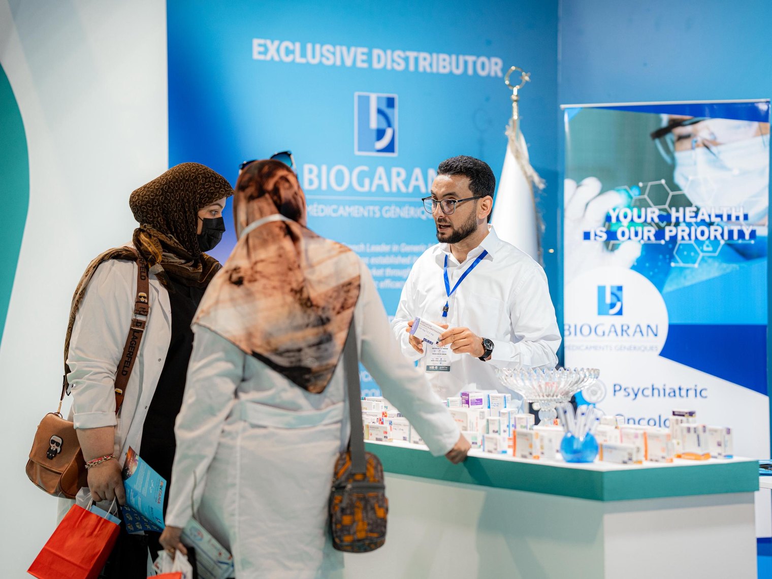 Un membre de l'équipe présente un médicament à deux visiteuses devant le mur Exclusive Distributor Biogaran